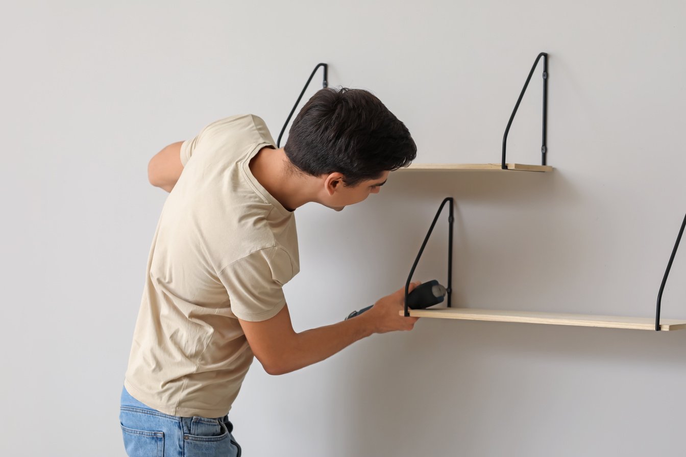 Young Man Installing Modern Shelves in Room